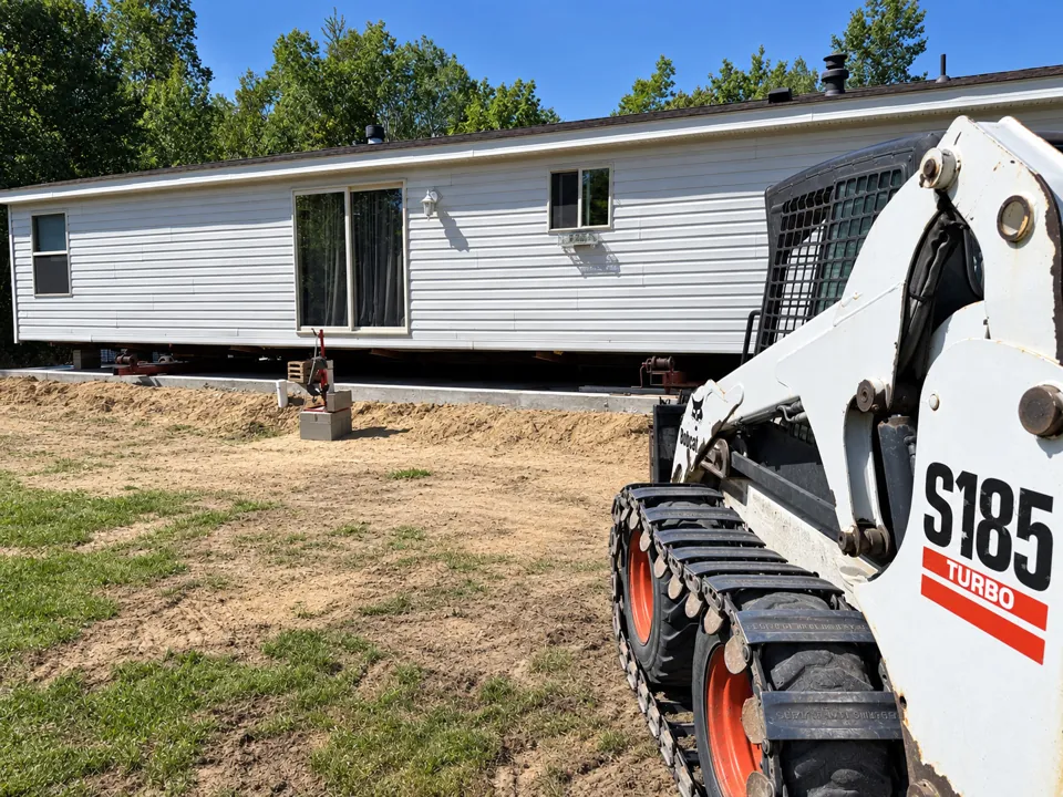 Manufactured home on site with a tracked skid steer in the foreground